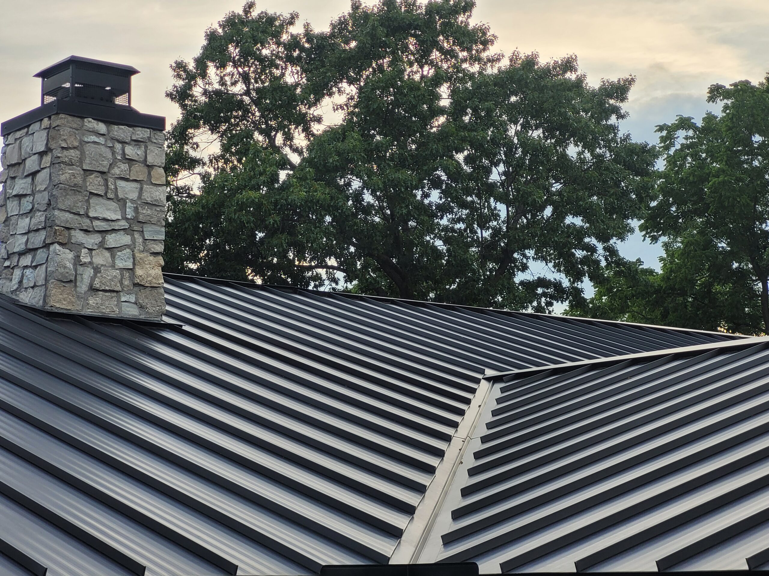 View of metal roof valley on a standing seam metal roof with a rock chimney